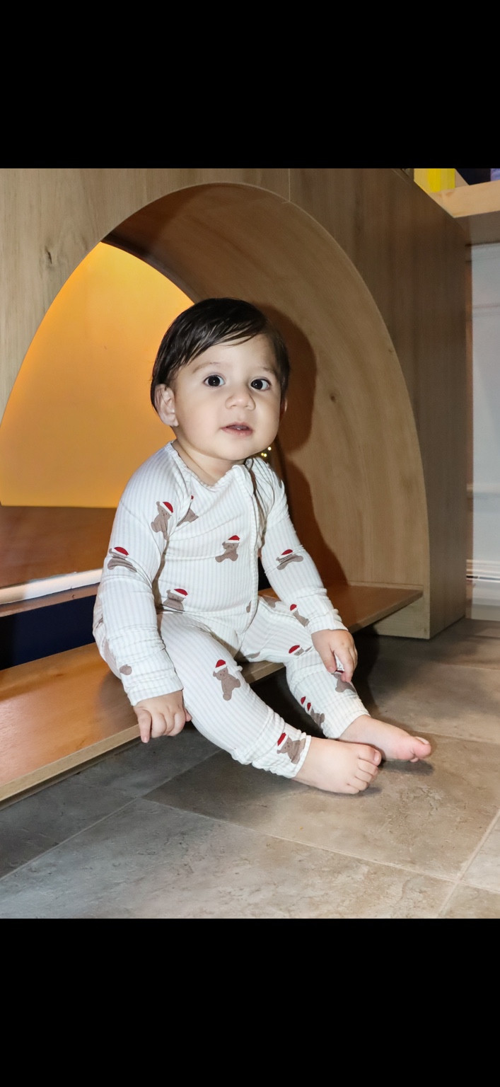 Baby in striped holiday pajamas sitting on a wooden bench