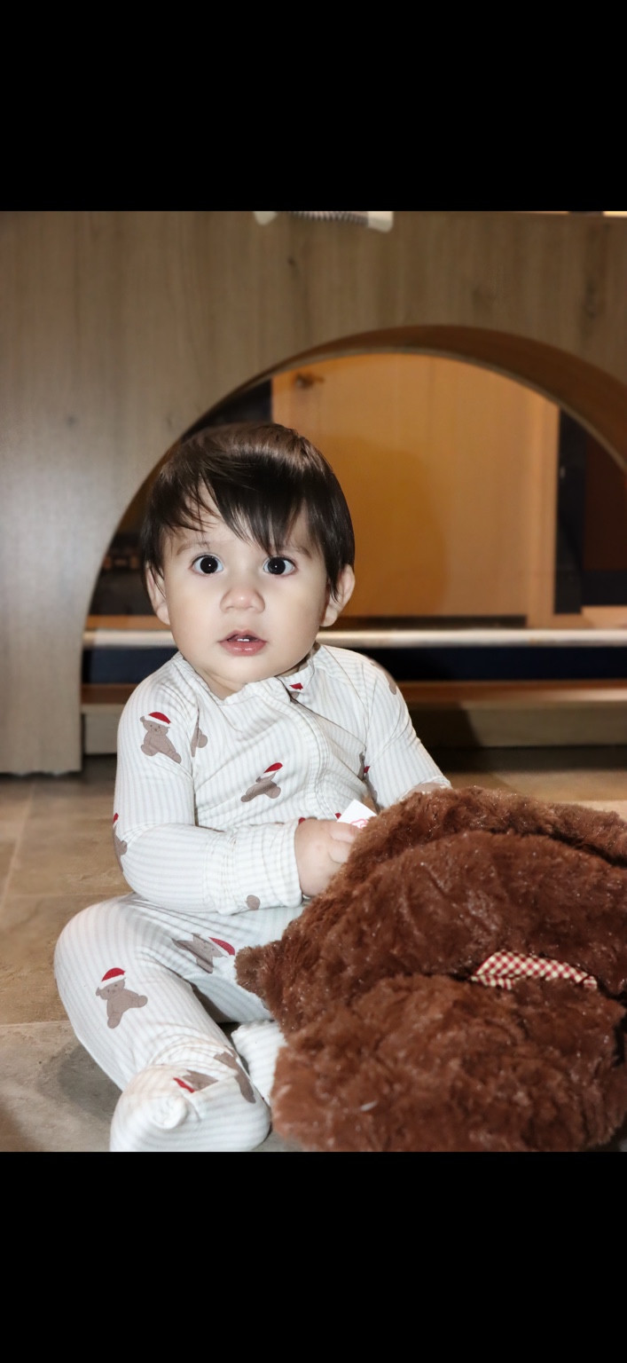 Baby in striped holiday pajamas sitting beside a brown teddy bear